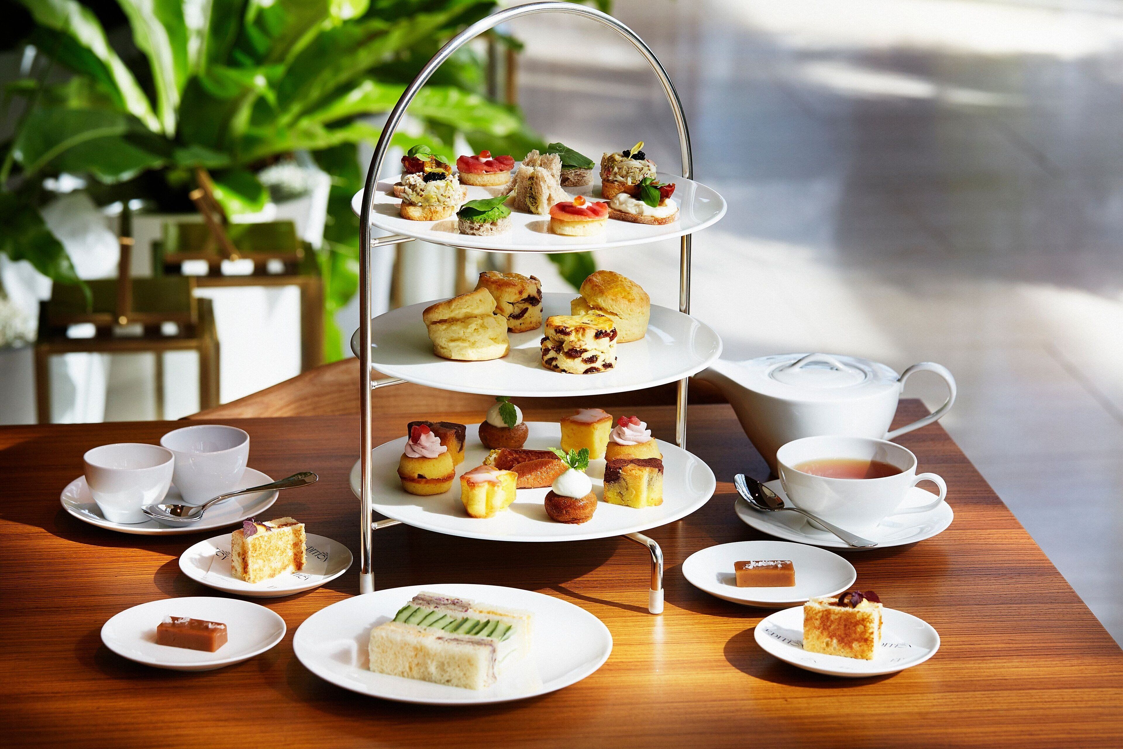 A three-tiered dessert stand with various pastries and cakes, accompanied by cups of tea and a teapot on a wooden table.