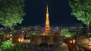 An outdoor dining area with a view of the Eiffel Tower at night, surrounded by greenery and city lights. - The Tokyo EDITION, Toranomon (Tokyo)