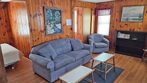 Ein gemütliches Zimmer mit Holzwänden, einer Couch, einem Sessel und einem Kamin.