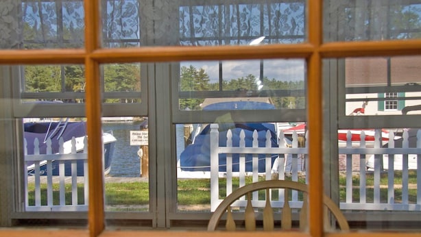 Blick durch ein Fenster mit weißem Zaun, einem blauen, mit Plane abgedeckten Gegenstand und einem Schild, das vor Störung der Enten warnt.