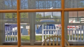 Blick durch ein Fenster mit weißem Zaun, einem blauen, mit Plane abgedeckten Gegenstand und einem Schild, das vor Störung der Enten warnt.