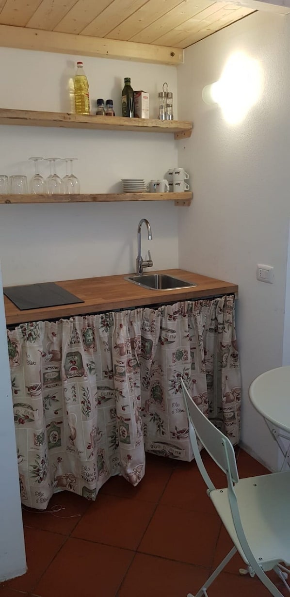 A small kitchen with a wooden countertop, a sink, and a window above the counter. There are shelves above the counter holding various items.