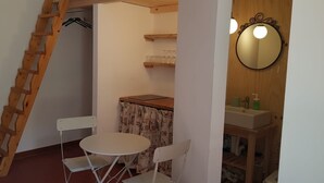 A small room with a wooden ladder, a white table, a chair, a mirror, and a shelf with glasses. - Nido del Corso apartment (Pontedera)