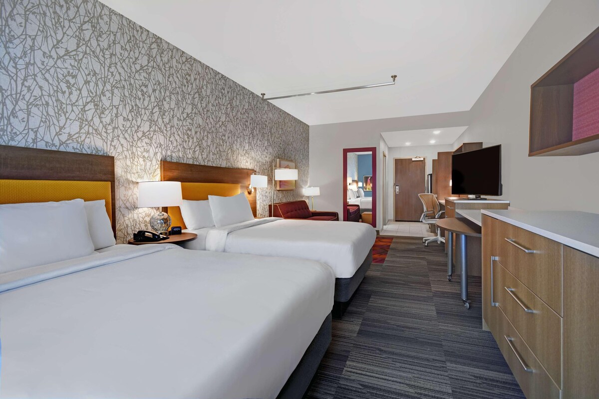 Habitación de hotel con dos camas, un escritorio, televisor y baño a la vista.