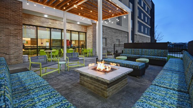An outdoor patio area with seating, a fire pit, and string lights. - Home2 Suites by Hilton Liberty NE Kansas City (Liberty)