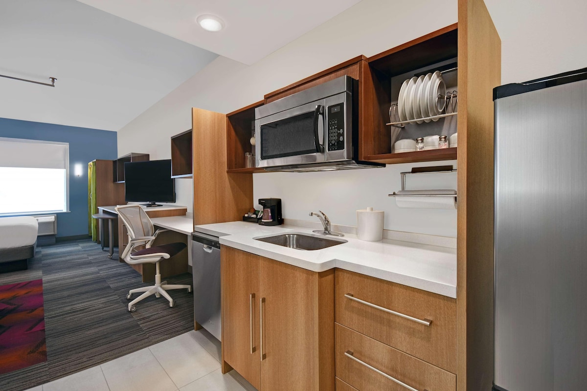 A modern kitchen with wooden cabinets, a stainless steel refrigerator, a microwave, and a coffee maker.