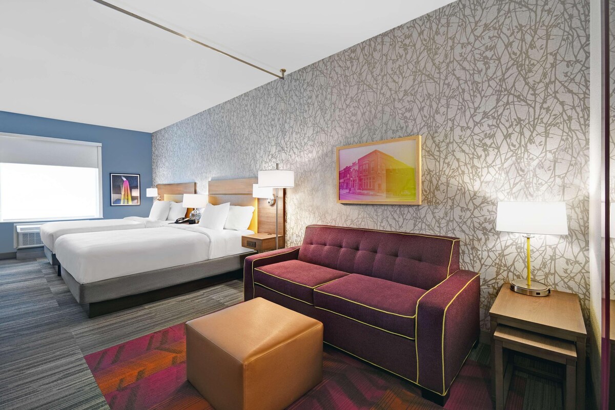 A hotel room with a large bed, a sofa, a small table, and a lamp.