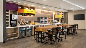 A modern kitchen area with a long counter, multiple appliances, and a dining table with chairs. - Home2 Suites by Hilton Liberty NE Kansas City (Liberty)
