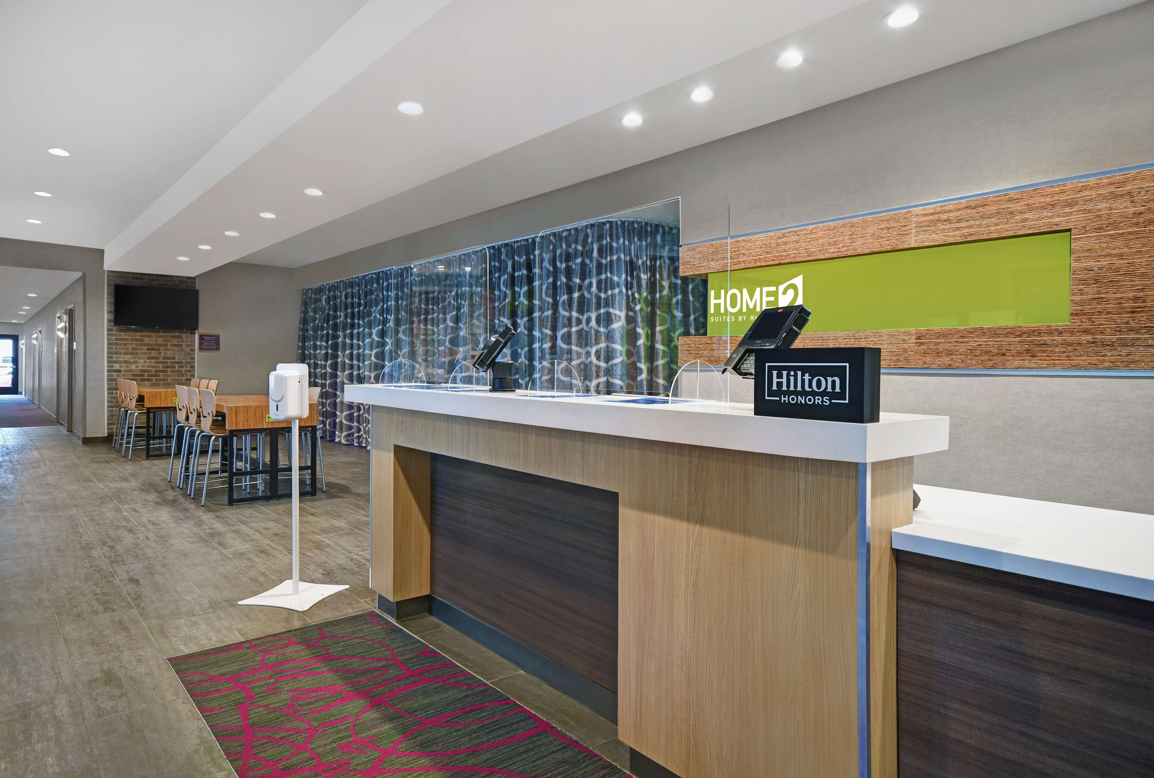 A modern hotel reception area with a counter, seating, and a large screen displaying the hotel's name.