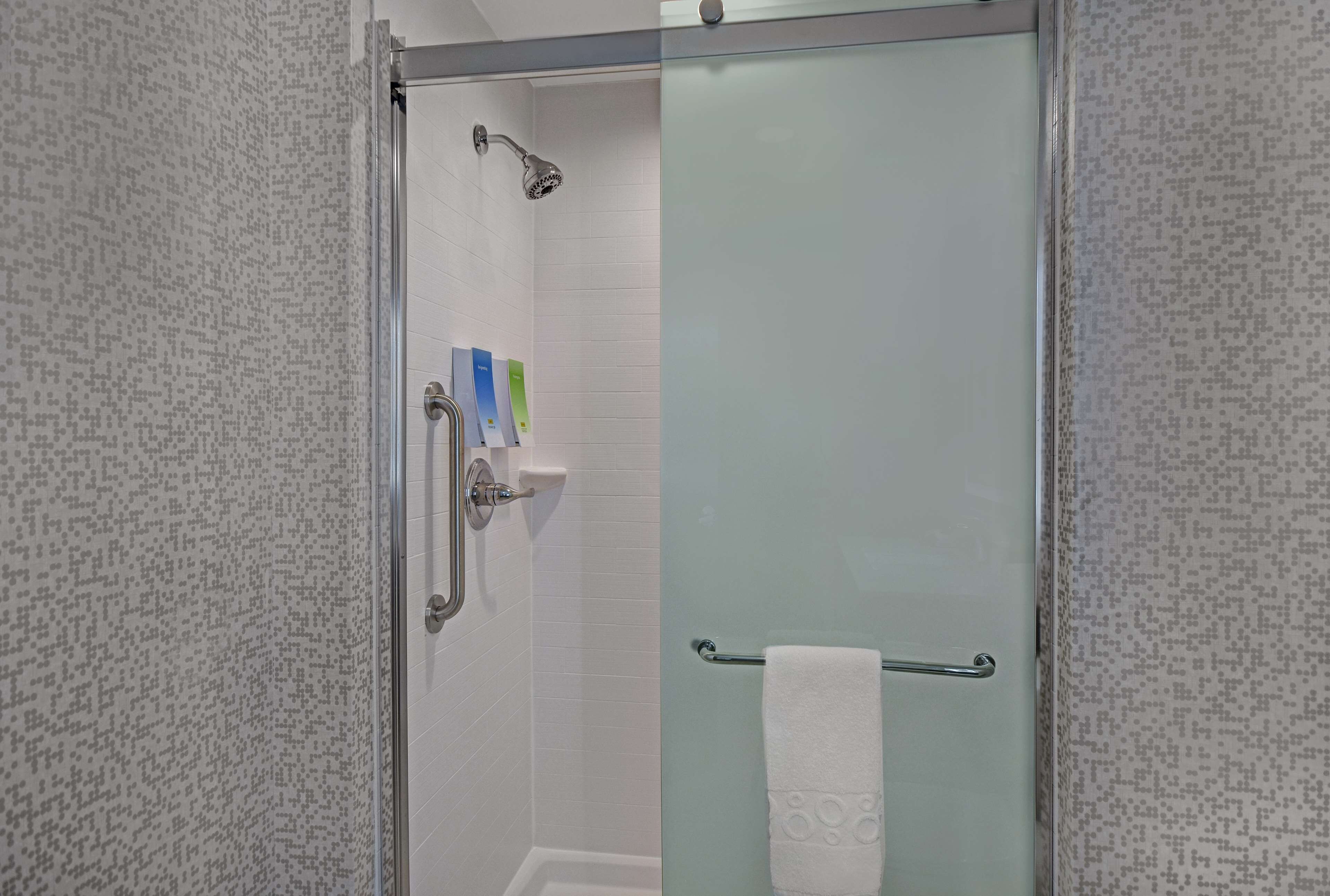 A glass-enclosed shower with a handheld showerhead, a towel rack, and a soap dispenser.