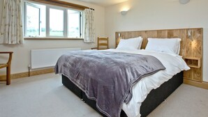 A bedroom with a large bed, a wooden headboard, a window with curtains, a radiator, and a bedside table with a lamp. - 3 bedroom accommodation in Cheriton, near Lynton (Cheriton, near Lynton)