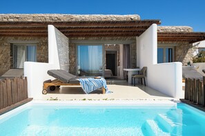 A poolside area with a lounge chair, a table, and a view of a stone building. - Aegean Hospitality Mykonos (Mykonos)