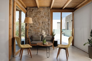 Une piÚce avec un mur en pierre, des poutres en bois au plafond, un canapé, deux fauteuils, une table et une lampe.