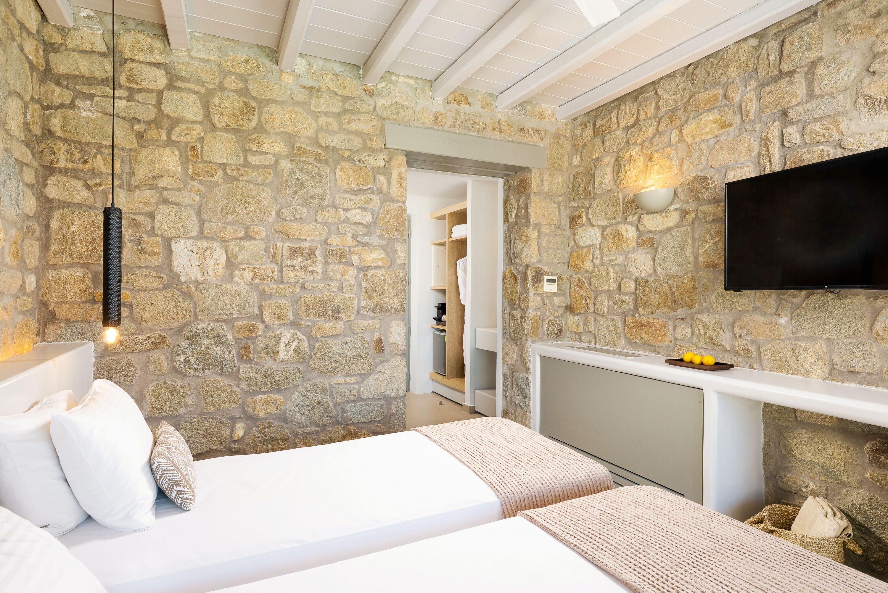 A bedroom with stone walls, a bed, a TV, and a small shelf with items.