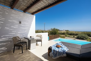A patio with a pool, a table, and chairs, overlooking a landscape with vegetation and a clear sky.