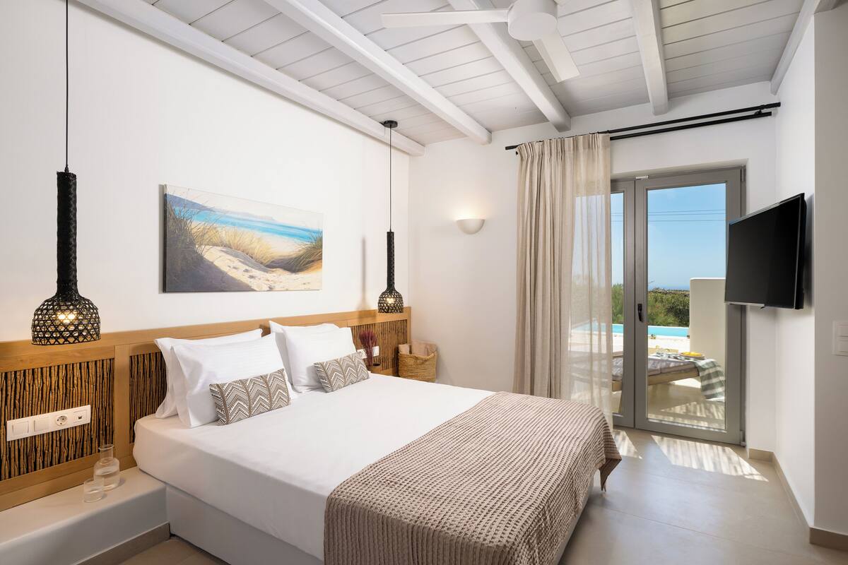 Ein Schlafzimmer mit Bett, Fernseher, einem Gemälde und einem Balkon mit Blick.