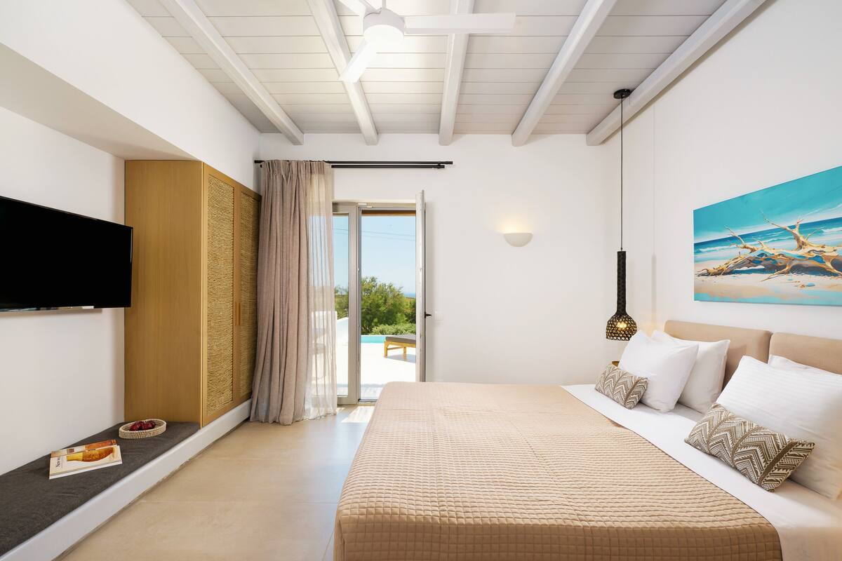 Ein Schlafzimmer mit Bett, Fernseher, einem Gemälde und Blick ins Freie.