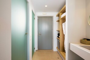 A narrow hallway with a door at the end, a wooden shelf with towels, and a small basket on the wall. - Aegean Hospitality Mykonos (Mykonos)