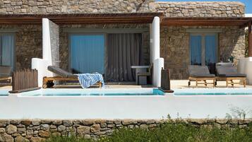 Un edificio de piedra con piscina, sillones de descanso y una mesa con mantel a rayas.