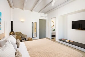 A bedroom with a bed, a sofa, a chair, a TV, and a mirror. - Aegean Hospitality Mykonos (Mykonos)