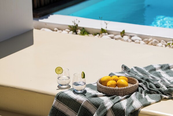 Zona de piscina con una bañera blanca, dos vasos de agua con lima y una cesta de limones.