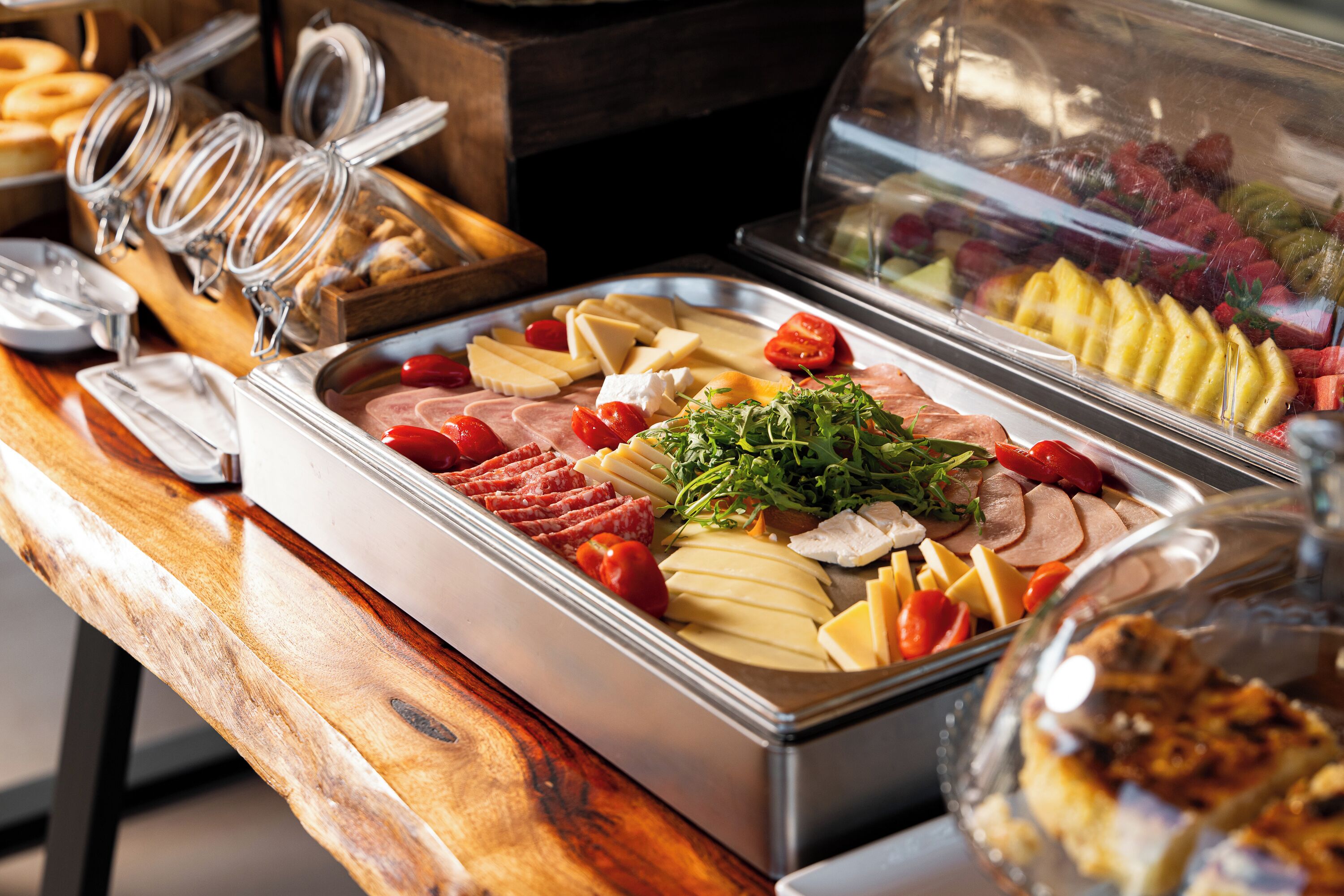 A buffet with various food items including meats, cheeses, and fruits.