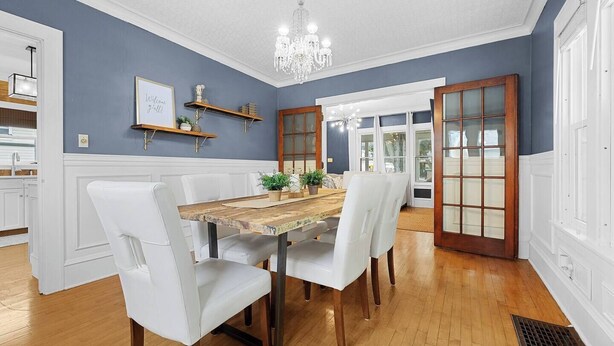 Comedor con mesa de madera, sillas blancas, lámpara de araña y pared decorada en azul.