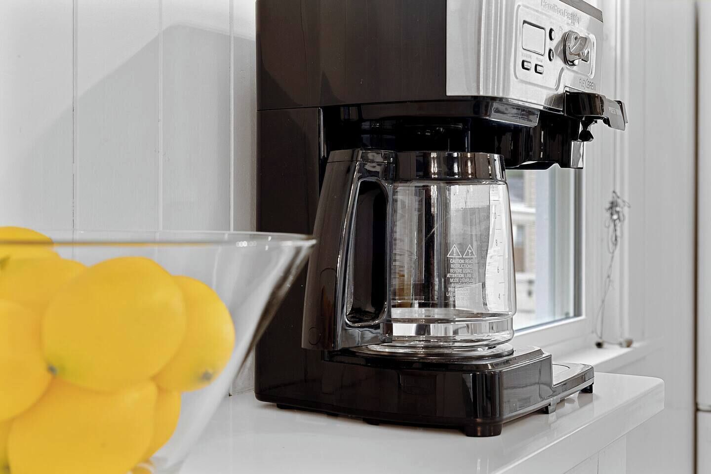 A black coffee maker on a white countertop with a clear glass carafe.