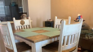 Een eettafel met een groen en bruin geruit tafelkleed, omringd door vier witte stoelen met donkere kussens.