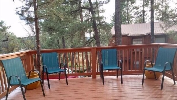 Een houten terras met drie blauwe stoelen en een geel kussen.