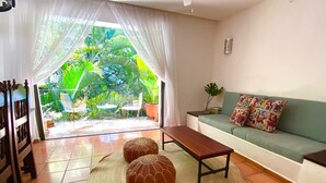 A living room with a sofa, two decorative stools, a bench, and a view of a garden through a glass door. - MARBELLA IN THE SPOTLIGHT, near the beach, for an effortlessly warm stay.  (Villa Las Flores)