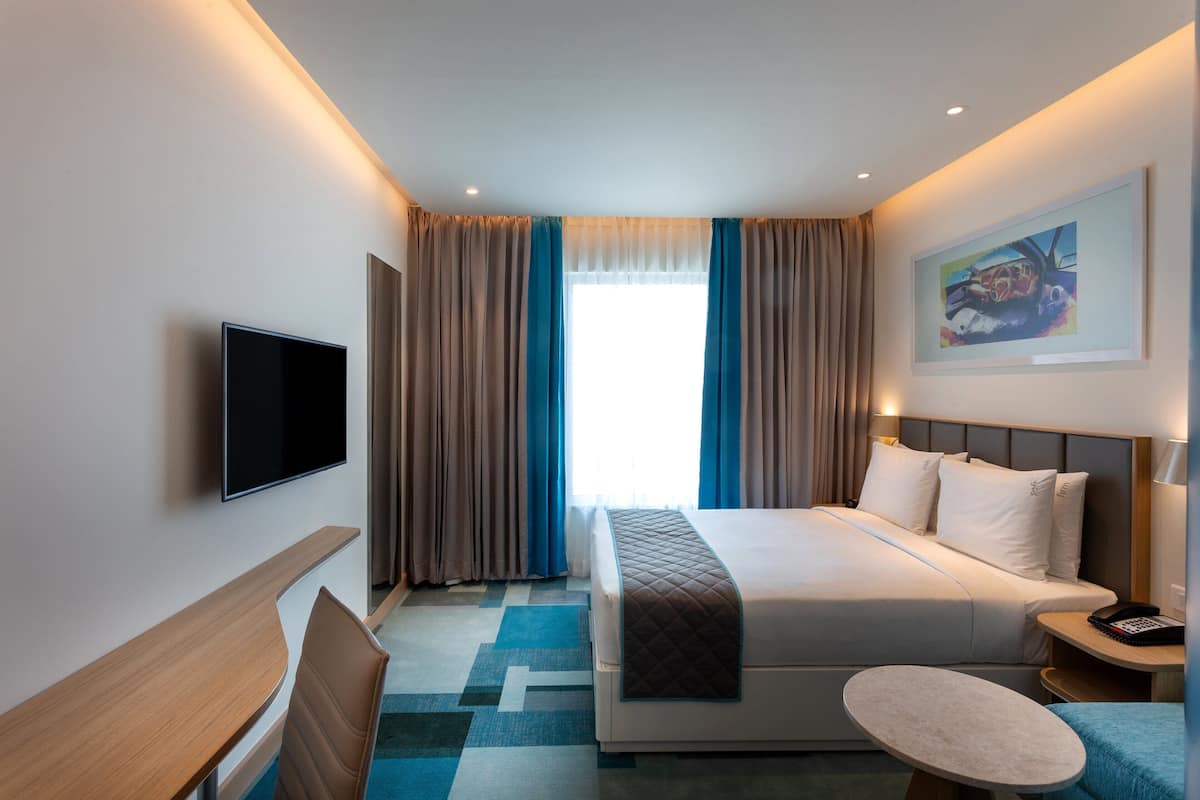 Habitació d'hotel amb llit, escriptori, cadira, televisió i finestra amb cortines.