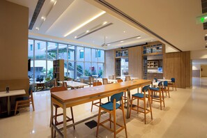 A modern dining area with wooden tables and chairs, large windows, and a view of the outside.