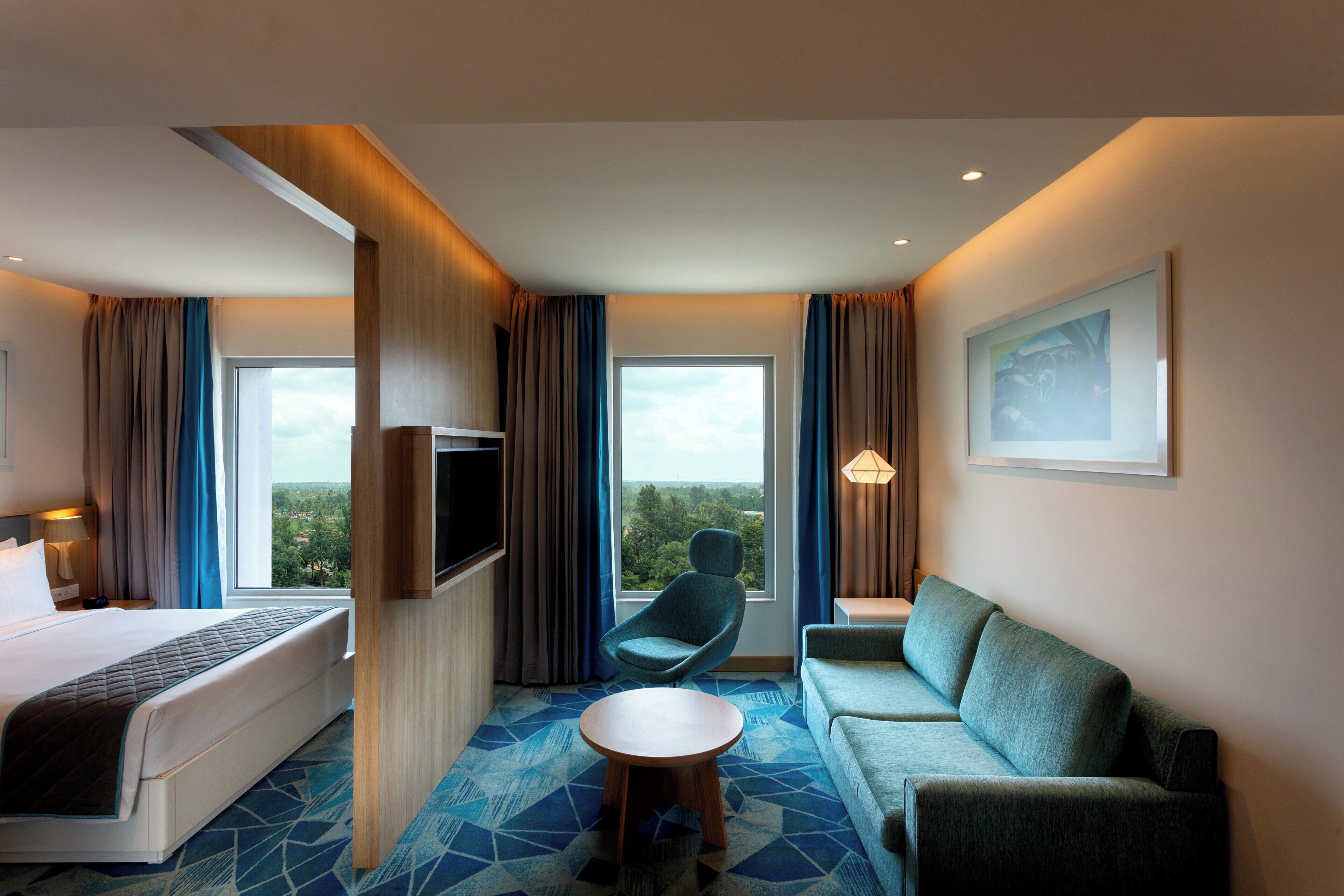 A hotel room with a bed, a sofa, a TV, a chair, and a small table.