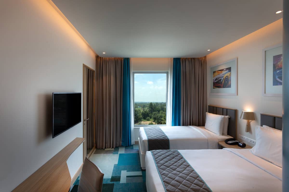 Habitació d'hotel amb dos llits, televisió, escriptori i finestra amb cortines.