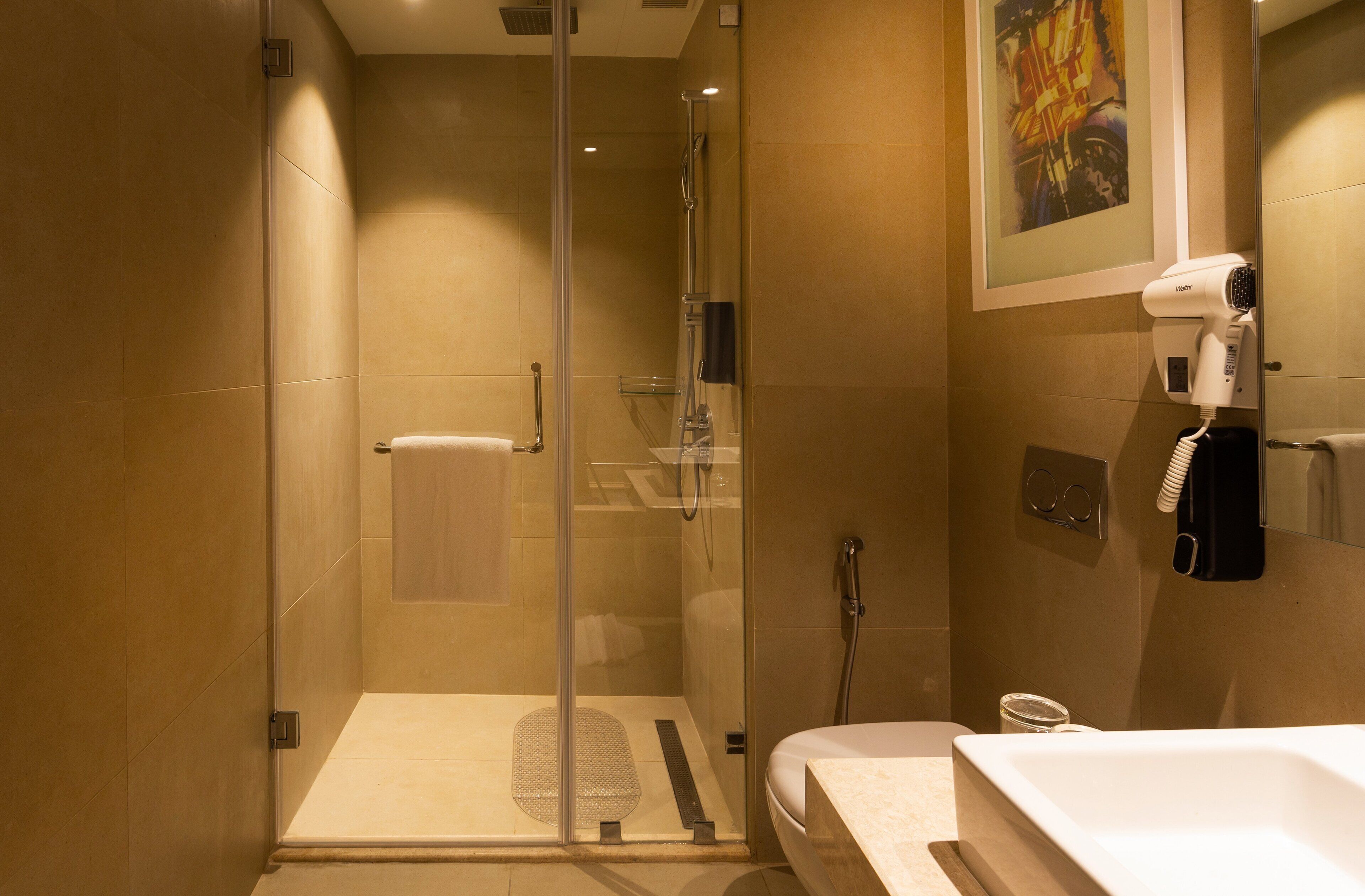 Een moderne badkamer met een douche met glazen wand, een witte wastafel en een aan de muur bevestigde haardroger.