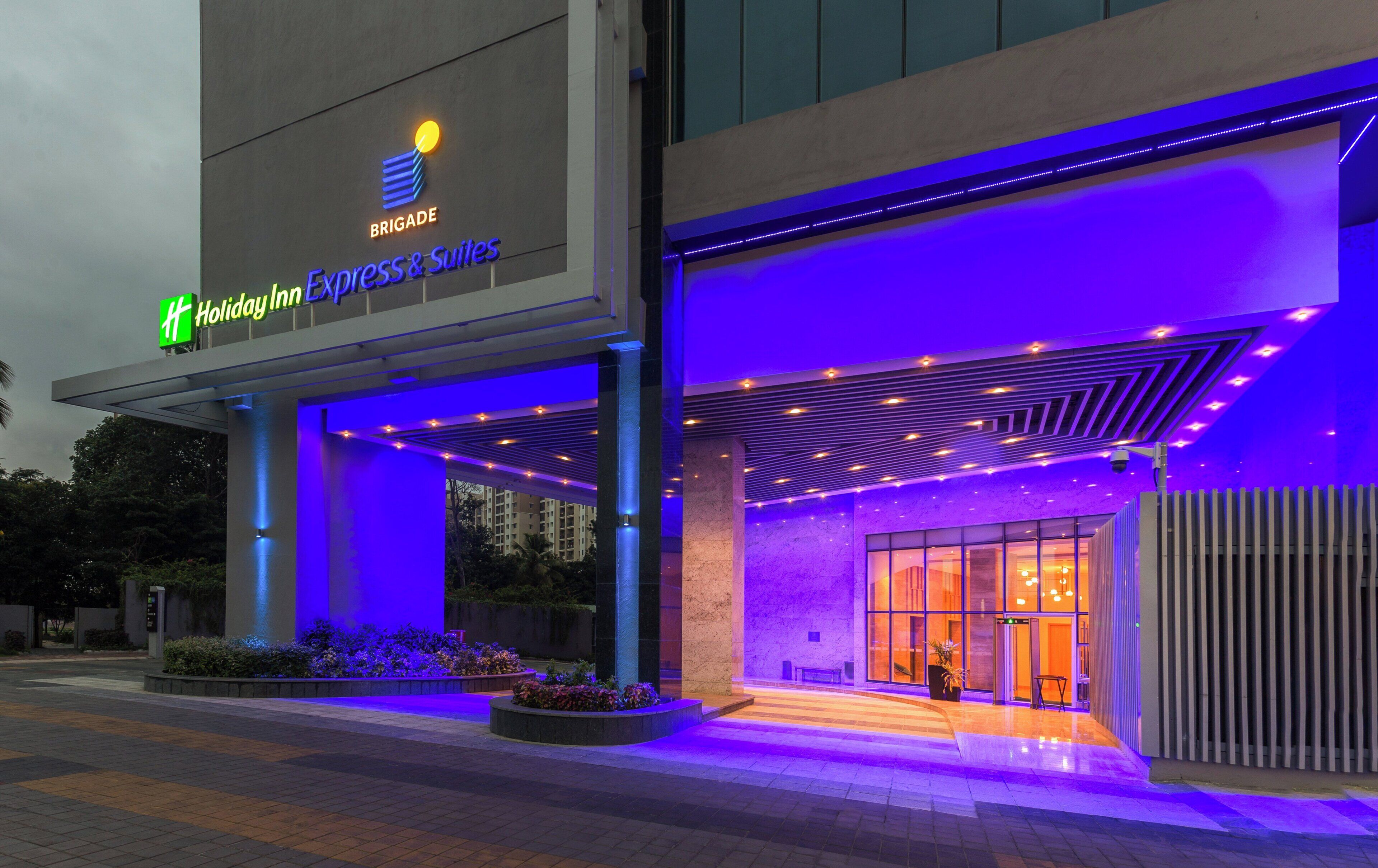 A hotel entrance with a modern design, featuring a prominent sign for 'Holiday Inn Express & Suites' and a well-lit facade.