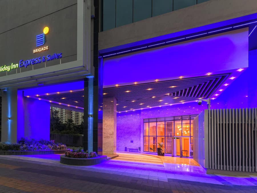 Una entrada de hotel con diseño moderno, destacando un cartel llamativo de 'Holiday Inn Express & Suites' y una fachada bien iluminada.