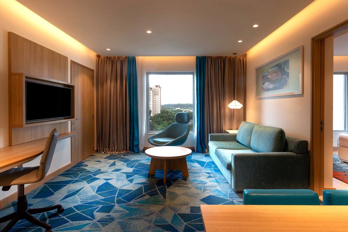 Habitació d'hotel moderna amb un gran finestral, un televisor de pantalla plana, un sofà, una cadira i una taula petita.