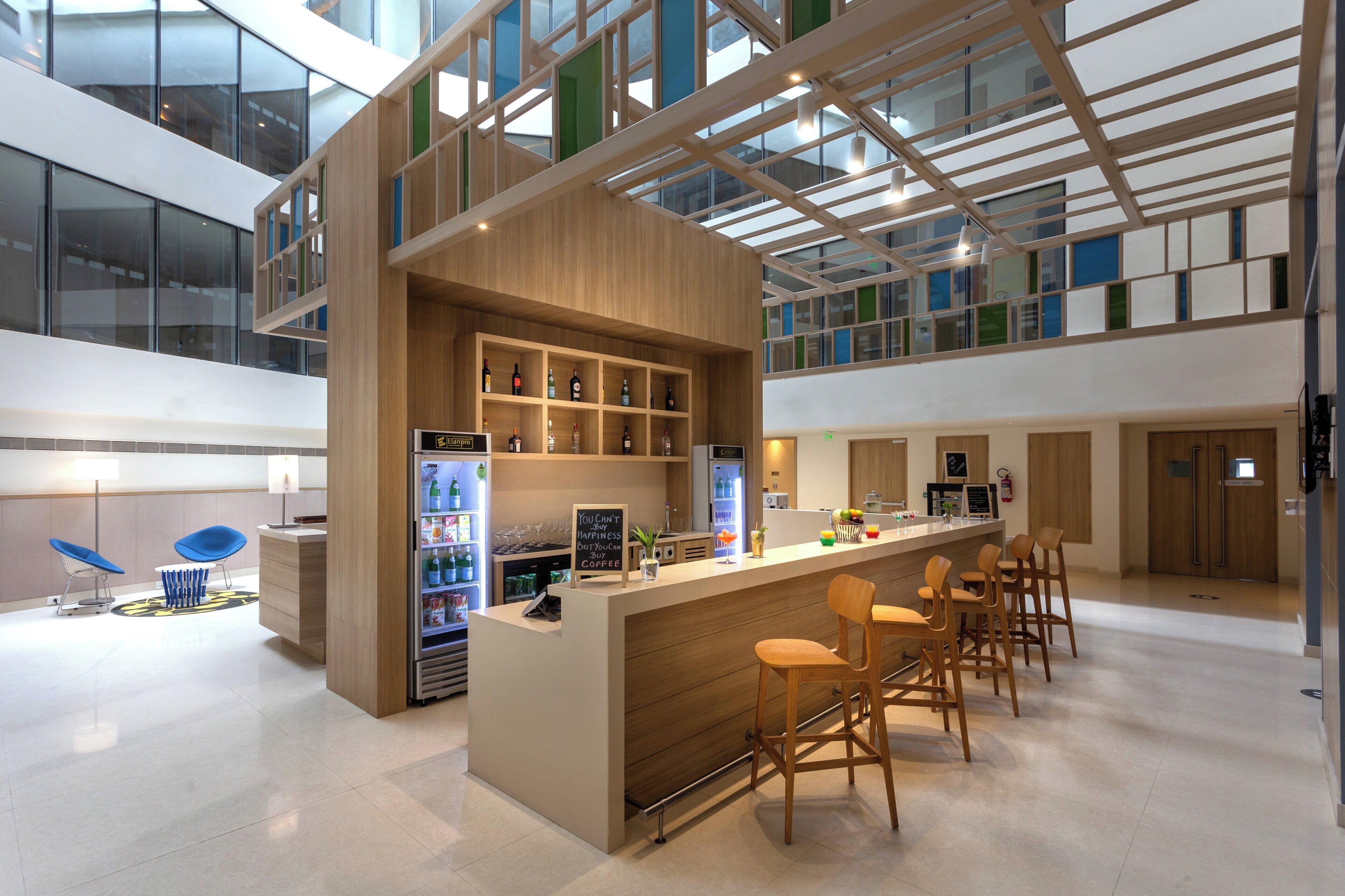 A modern bar area with a wooden counter, seating, and a view of the upper floor through a glass ceiling.