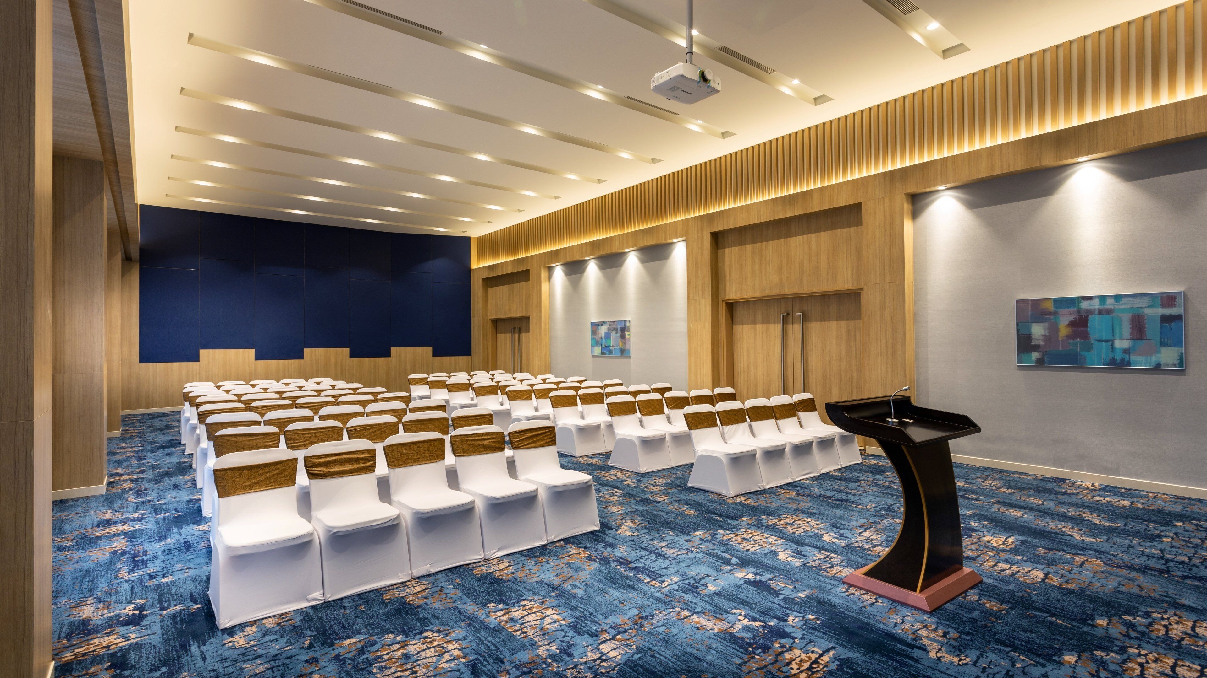 A conference room with rows of chairs, a podium, and a projector on the ceiling.