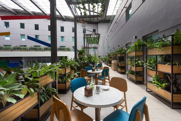 A modern indoor space with multiple seating areas, wooden planters with greenery, and a high ceiling with skylights. - Holiday Inn Express & Suites Bengaluru Old Madras Road by IHG (Bengaluru)