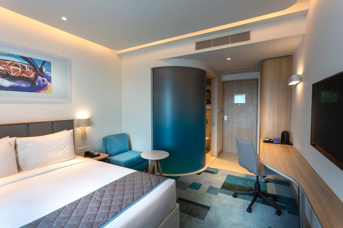 Habitació d'hotel amb llit, escriptori, cadira, taula petita, paret decorada de blau i un quadre penjat a la paret.