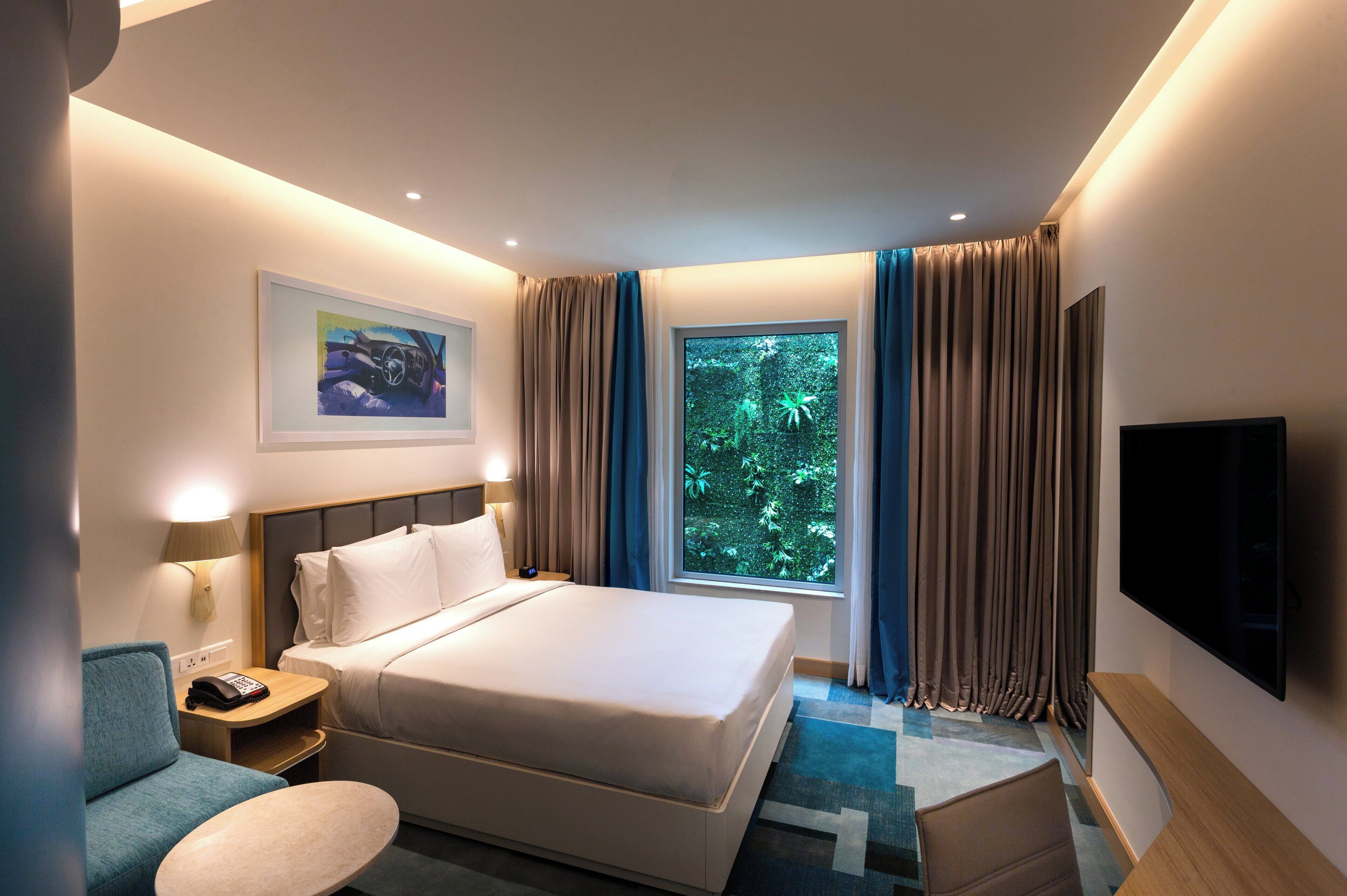 A hotel room with a bed, bedside tables, a desk, a chair, a TV, and a window with curtains.