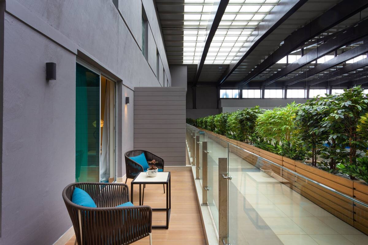 Un espai interior modern amb un balcó, zona de seients i una filera de plantes al llarg de la barana.