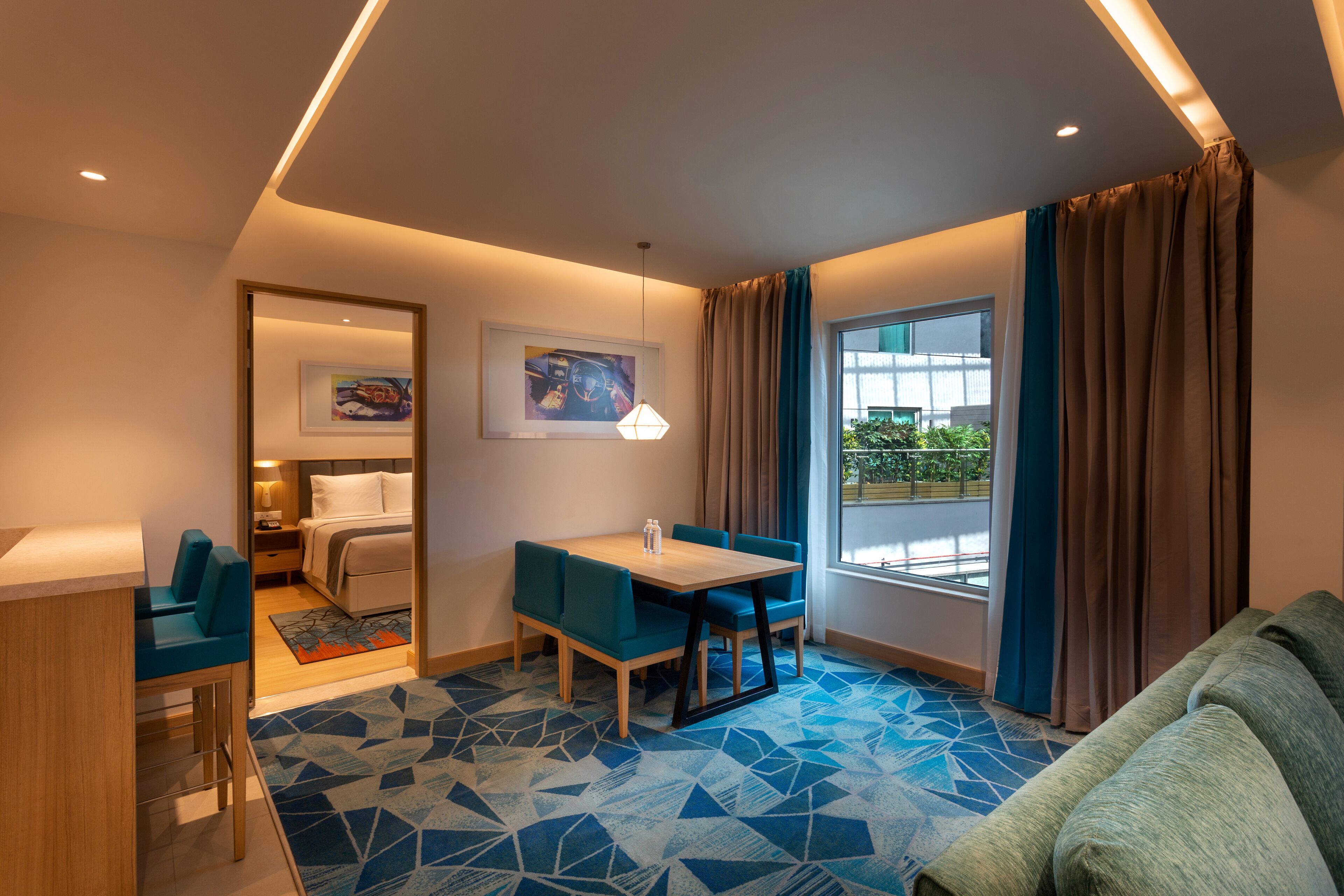 A modern hotel room with a dining area, a bed, a sofa, and a large window with curtains.