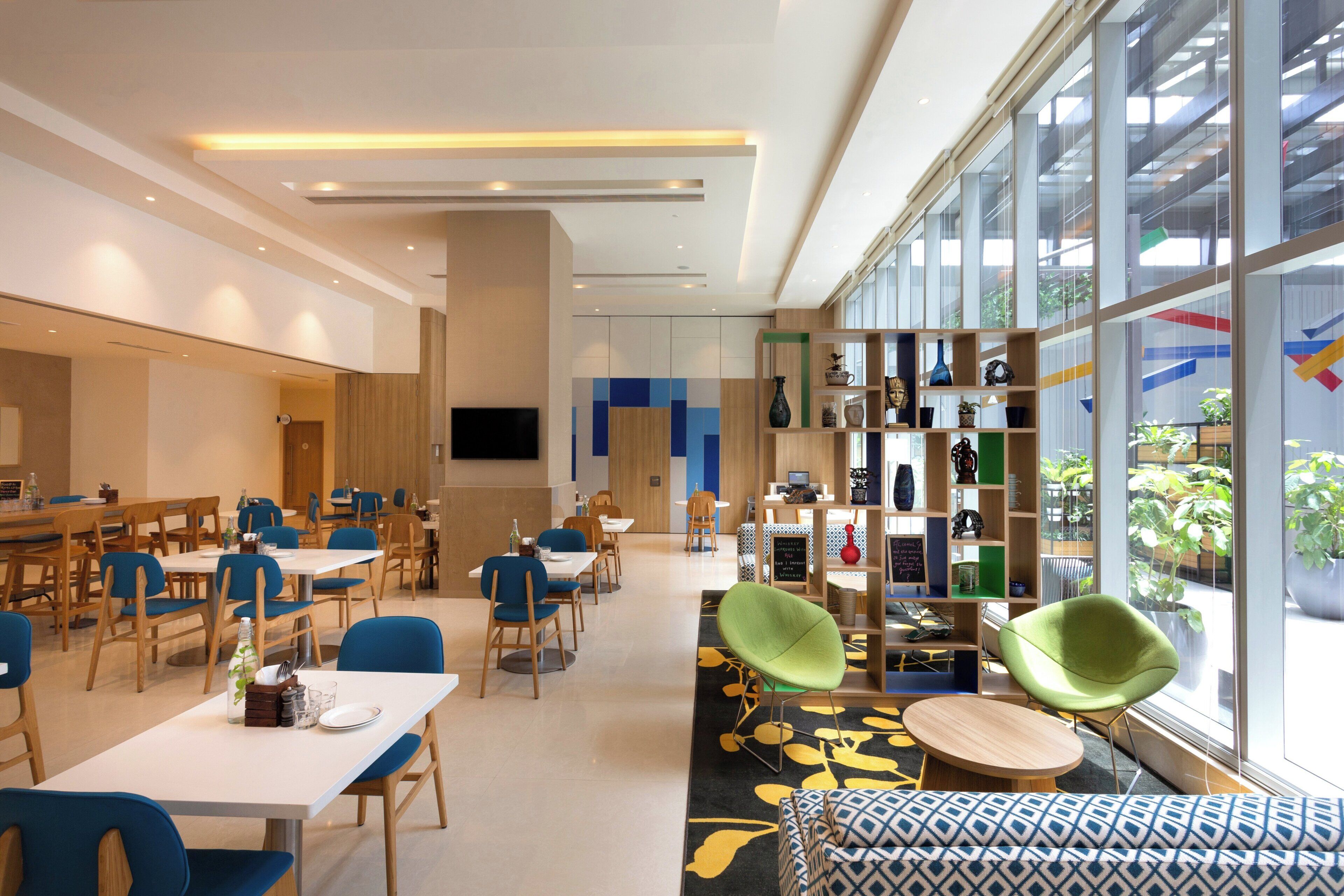 Un'area pranzo moderna con tavoli e sedie, una grande finestra con vista e una libreria piena di oggetti.