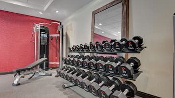 Un gimnasio con una prensa de banca, mancuernas y un espejo.