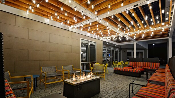 An outdoor patio area with a fire feature, seating, and a ceiling with exposed beams and string lights. - Home2 Suites by Hilton Fort Mill, SC (Fort Mill)