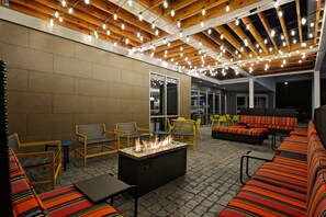 An outdoor patio area with a fire feature, seating, and a ceiling with exposed beams and string lights. - Home2 Suites by Hilton Fort Mill, SC (Fort Mill)